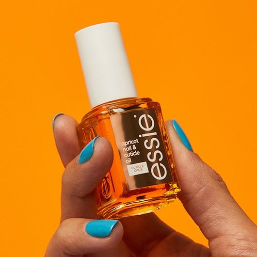 Hand with blue manicure holding Essie apricot nail and cuticle oil in classic format
